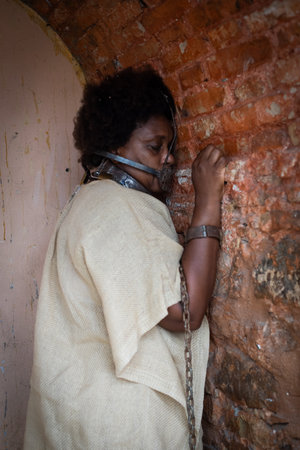 Portrait of a black woman chained and with an iron mask stuck in her mouth, leaning against a brick wall. Slavery in Brazil. Feelings of fear and sadness.の写真素材