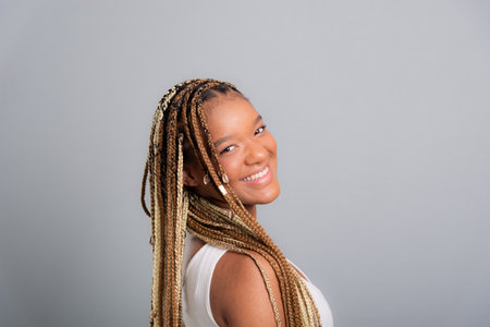 Beautiful brunette woman with braids in her hair wearing jeans and white shirt looking and smiling at the camera. Isolated on gray studio background.の写真素材