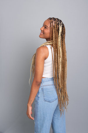 Beautiful brunette woman with braids in her hair wearing jeans and white shirt smiling and...