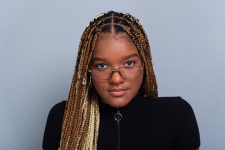 Beautiful brunette with braids in her hair, wearing jeans and a black blouse and wearing glasses. Concentrated and confident person. Isolated on a gray background.の写真素材