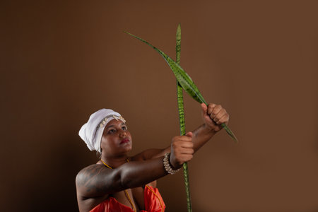 Salvador, Bahia, Brazil - October 21, 2024: Woman in traditional Candomble clothing, holding the Espada de Sao Jorge plant and posing for a photo.の写真素材