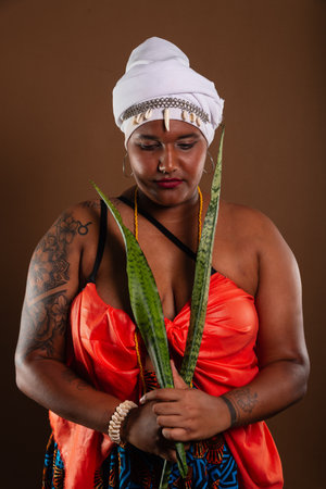 Salvador, Bahia, Brazil - October 21, 2024: Woman in traditional Candomble clothing, holding the sword of Saint George plant against brown background. from inside. Salvador, Bahia.の写真素材