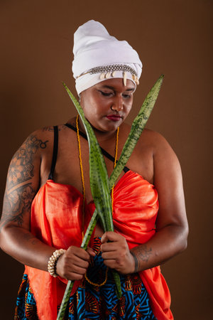 Salvador, Bahia, Brazil - October 21, 2024: Woman in traditional Candomble clothing, holding the sword of Saint George plant against brown background. from inside.の写真素材