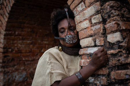 Black woman chained and with an iron mask on her mouth, representing the slave Anastacia on the brick walls of Pelourinho. Slavery in Brazil. Suffering and pain.の写真素材
