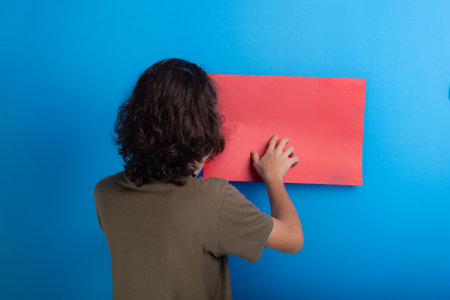 young black haired man holding an empty red poster with his back to the camera on a blue background.の写真素材