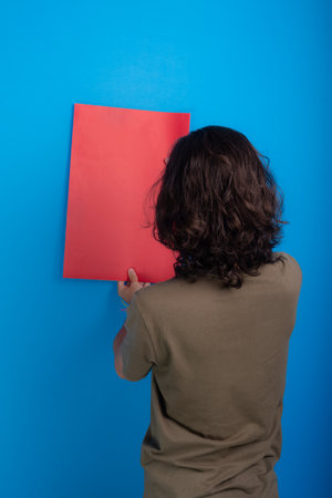 young black haired man holding an empty red poster with his back to the camera on a blue background.の写真素材