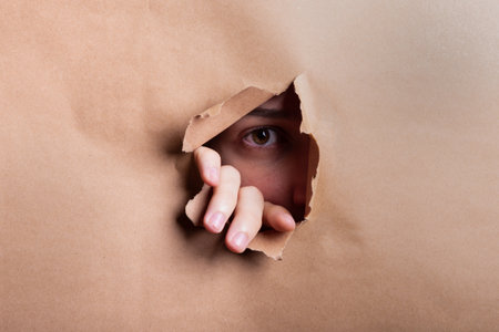 Man eye looking through a hole in a sheet of paper. Studio portrait.の写真素材