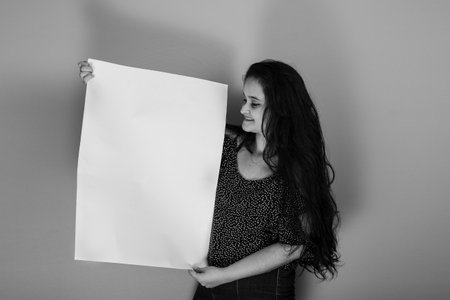 Beautiful black haired latin american woman holding blank banner with confident face, standing. Isolated on mustard colored background.の写真素材