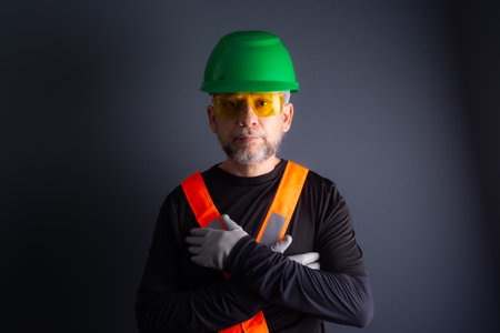 Photo of a civilian worker wearing a green helmet, reflective vest and protective glasses. isolated on gray background. Construction worker.の写真素材