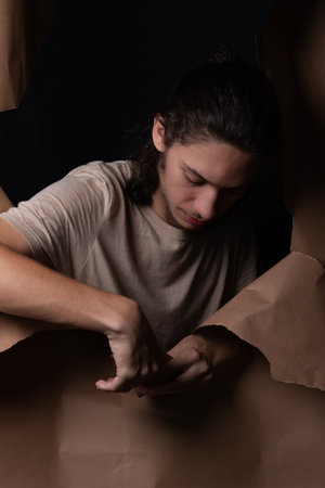 A man peering through a hole in a sheet of brown paper. Tearing the paper with his hands. Studio portrait.の写真素材
