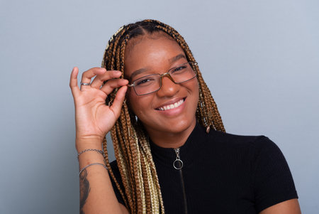 Beautiful brunette with braids in her hair, wearing jeans and a black blouse and wearing glasses. Concentrated and confident person. Isolated on a gray background.の写真素材