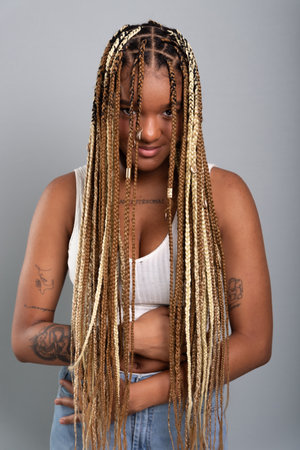 Close-up portrait of brunette woman with braids in her hair, looking at camera with hands on her belly. Isolated on gray studio background.の写真素材