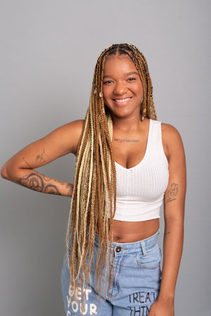 Beautiful brunette woman with braids in her hair wearing jeans and white shirt looking and smiling...