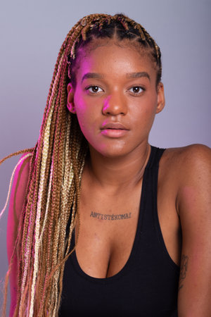 Brunette model with braids in her hair, wearing a black blouse and looking at the camera. Confident and calm person. Isolated on gray background.の写真素材