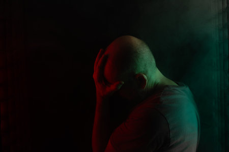 Bald and bearded man, head down. Studio portrait with black background and colored lights.の写真素材