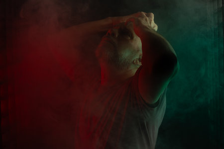 Bald and bearded man making despair gesture with hand. Isolated on smoky black background with colored lights.の写真素材