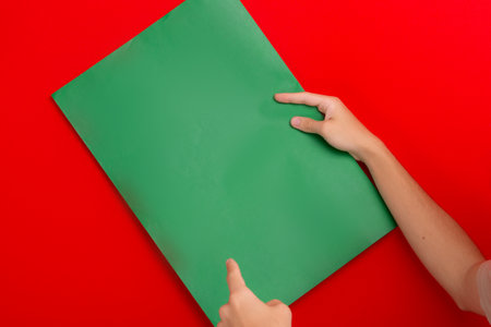 Hands holding green colored, empty poster, leaning against red background. advertisement concept.の写真素材