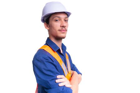 Young architect wearing white helmet and luminous vest posing for photo with arms crossed. Isolated...