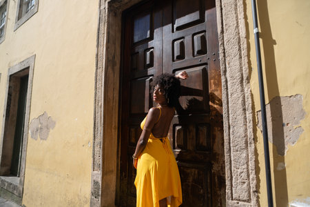 Portrait of beautiful woman wearing yellow dress standing by old brown wooden door. Happy person traveling concept.の写真素材