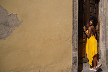 Portrait of beautiful woman wearing yellow dress standing by old brown wooden door. Happy person traveling concept.の写真素材