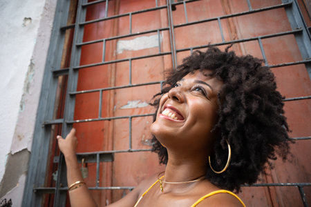 Close-up portrait of a woman wearing a yellow outfit with afro hairstyle, smiling, next to an iron fence. Confident and happy personの写真素材