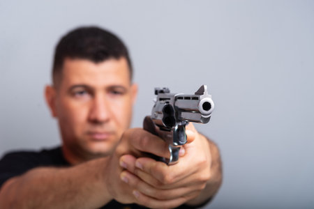 Studio portrait of a shooting instructor pointing a revolver to the side. isolated on gray...