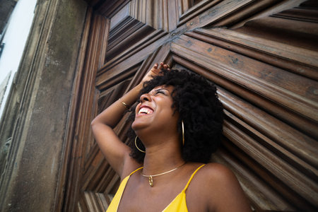 Close-up portrait of a woman wearing a yellow outfit, with afro hair, against a centuries-old wooden door. Confident person. Brazilの写真素材