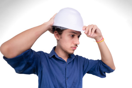 Studio portrait of young architect adjusting white helmet on head. Isolated on white background. Safety equipment.の写真素材