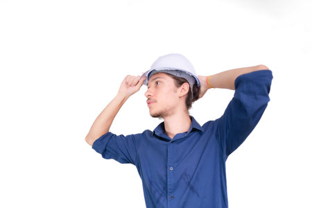 Studio portrait of young architect adjusting white helmet on head. Isolated on white background. Safety equipment.の写真素材