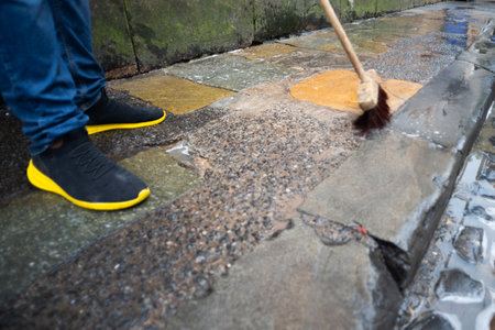 A person sweeping a sidewalk that is wet. Care and cleaning concept.