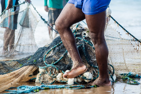 Half a body of unidentified fishermen collecting the fishing net after catching fish. Seafood, fishing as a hobby. Brazilの写真素材