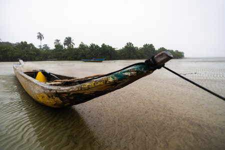 A fishing canoe anchored on the sand of a dry beach. Low tide. Rainy day with heavy clouds. Means of transport.の写真素材