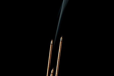 Three burning incense sticks with smoke on a black background. Studio shot.の写真素材