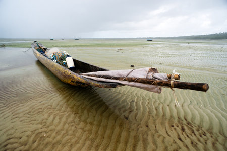 A fishing canoe anchored on the sand of a dry beach. Low tide. Rainy day with heavy clouds. Means of transport.の写真素材