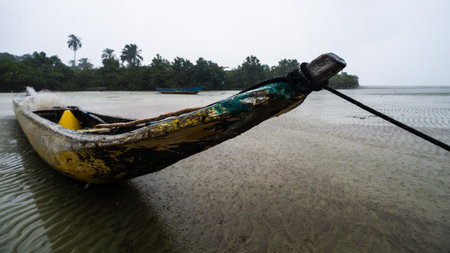 A fishing canoe anchored on the sand of a dry beach. Low tide. Rainy day with heavy clouds. Means of transport.の写真素材