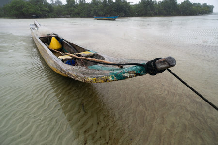 A fishing canoe anchored on the sand of a dry beach. Low tide. Rainy day with heavy clouds. Means of transport.の写真素材