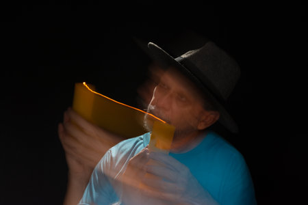 Artistic portrait of bearded bald man in blue shirt wearing hat making light trail. Motion blur. Black background.の写真素材