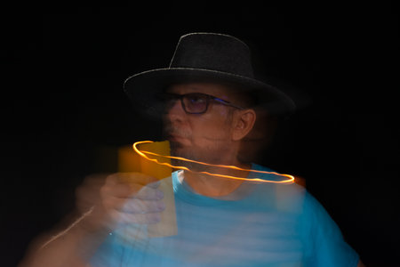 Artistic portrait of bearded bald man in blue shirt wearing hat making light trail with burning...