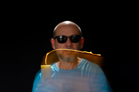 Artistic portrait of bearded bald man in blue shirt making motion blur effect with burning yellow...