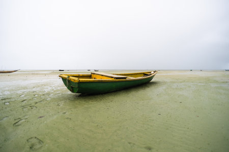 Fishing boat on the sand of a dry beach. Quite rainy day with dense clouds.の写真素材
