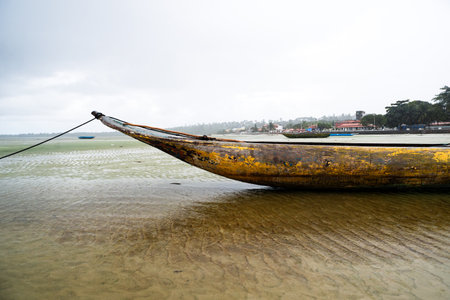 A fishing canoe anchored on the sand of a dry beach. Low tide. Rainy day with heavy clouds. Means of transport.の写真素材