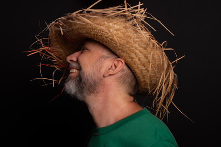 Smiling bearded man in straw hat and green shirt dressed up for Sao Joao festival in Brazil.の写真素材