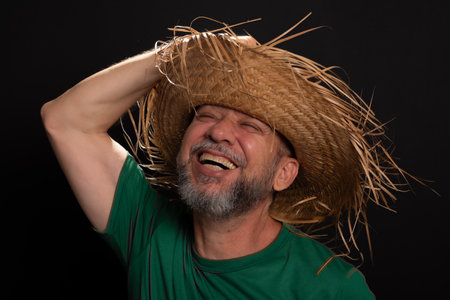 Smiling bearded man in straw hat and green shirt dressed up for Sao Joao festival in Brazil. country partyの写真素材