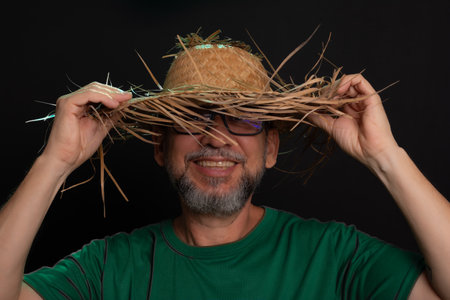 Smiling bearded man in straw hat and green shirt dressed up for Sao Joao festival in Brazil. country partyの写真素材