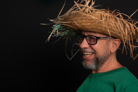 Smiling bearded man in straw hat and green shirt dressed up for Sao Joao festival in Brazil.の写真素材