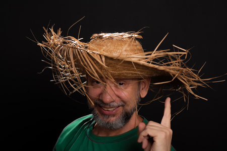 Smiling bearded man in straw hat and green shirt dressed up for Sao Joao festival in Brazil.の写真素材