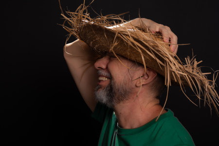 Smiling bearded man in straw hat and green shirt dressed up for Sao Joao festival in Brazil. country partyの写真素材