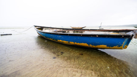 Fishing boat anchored on the sand of a dry beach. Quite rainy day with dense clouds. Means of...