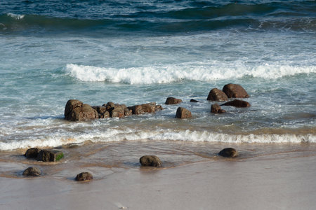 Dark rocks on the seashore of a beautiful beach. Waves breaking on the sand, paradise. Brazilの写真素材