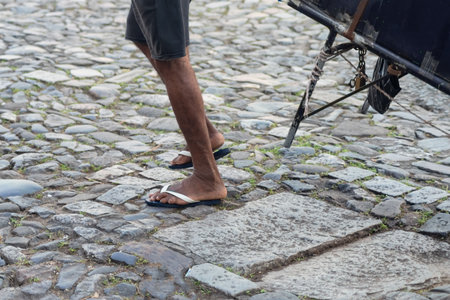 Half body of an unidentified person walking on a cobblestone street driving a handcart. Pedestrian...